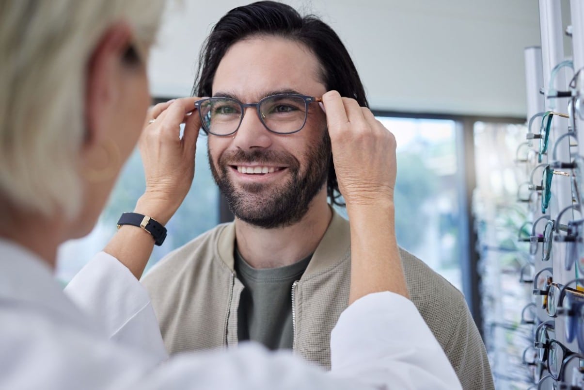 A man trying on glasses getting professional styling advice from optometrist.